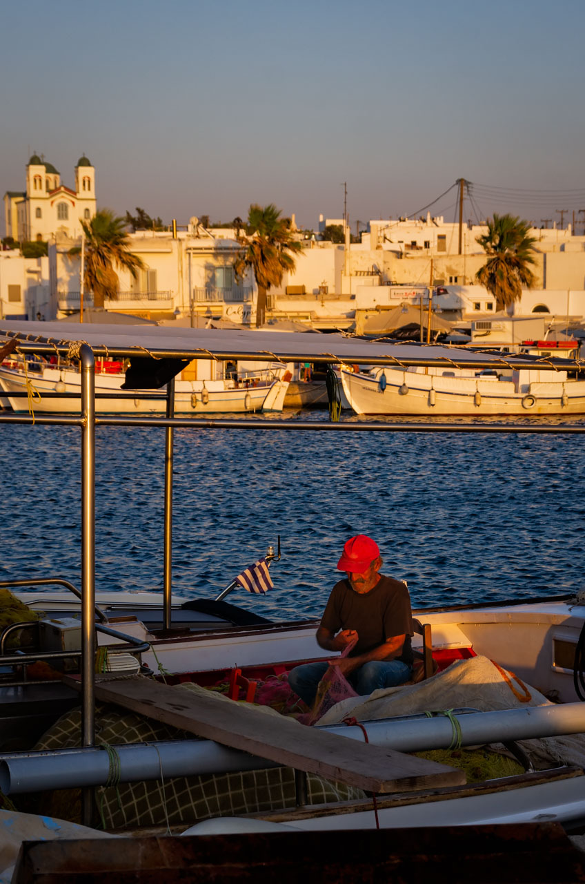 Pescatore rammenda le reti al porti di Naoussa al tramonto